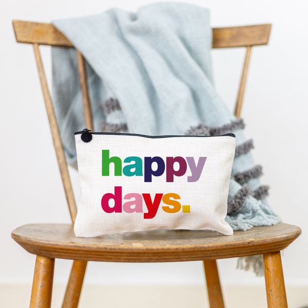 A white canvas make up pouch with contrasting black zip, printed with the phrase Happy Days in multi-coloured text